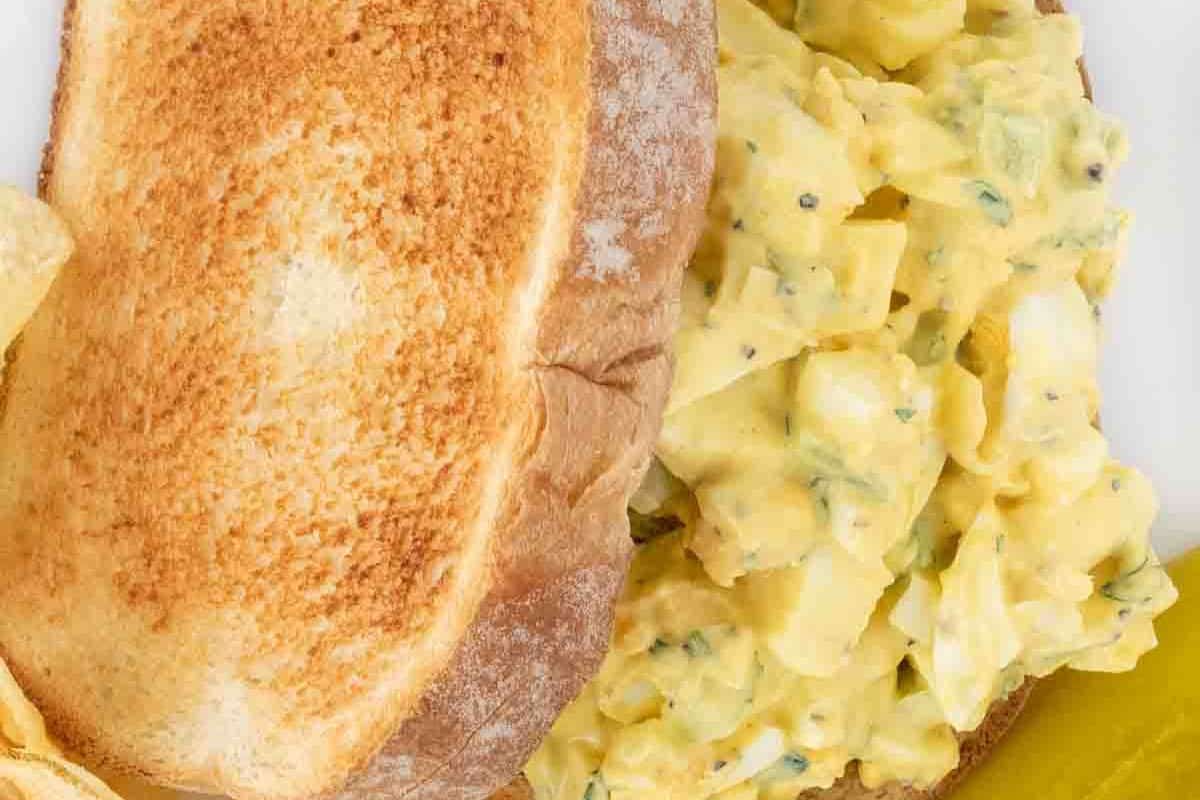 Enjoy a toasted sandwich filled with an easy egg salad recipe, perfectly paired with a side of potato chips and a crisp pickle.