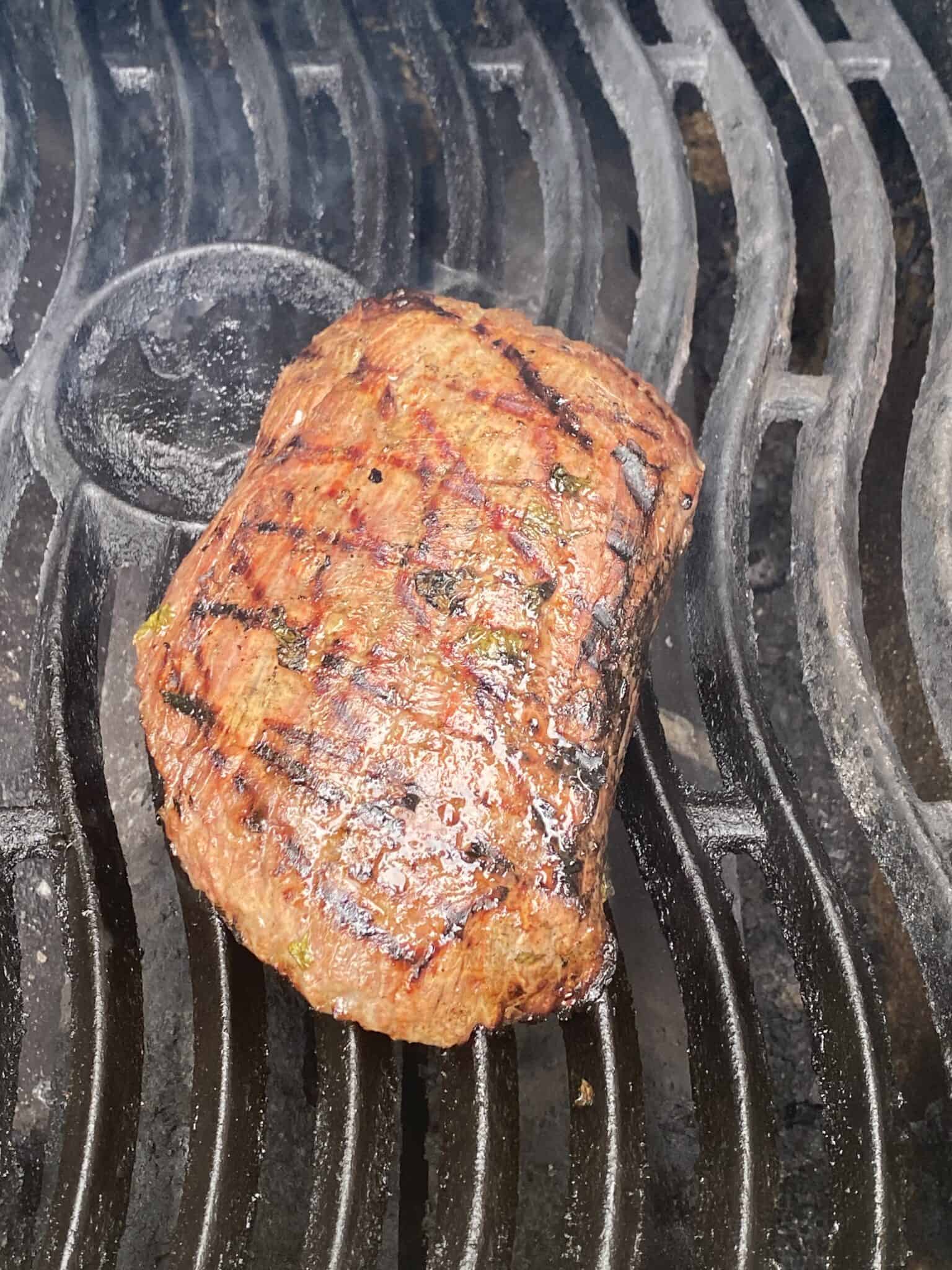 A piece of grilled steak with char marks, perfect for crafting mouth-watering street tacos, sizzles on a black metal grill.
