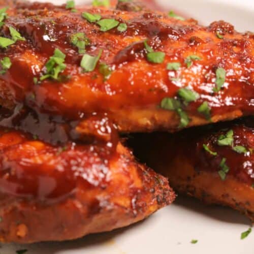 Instant Pot BBQ Chicken breasts coated in barbecue sauce and garnished with chopped fresh herbs on a white plate.