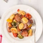 A white plate with dinner all topped with grated cheese. A fork rests on the plate beside the food.