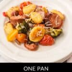 A white plate with roasted gnocchi, Italian sausage slices, tomatoes, broccoli, and bell peppers, topped with grated cheese. Text below reads: "One Pan Italian Sausage with Gnocchi"—a classic Italian Sausage with Gnocchi dish.