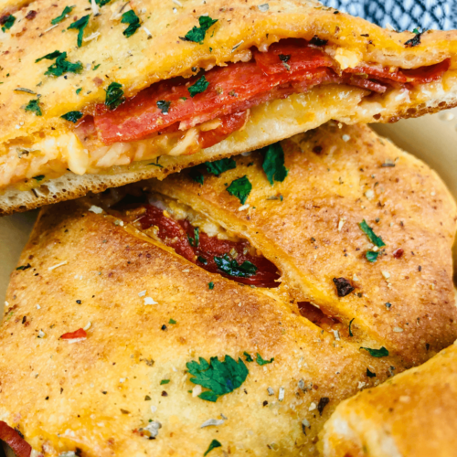 Close-up of a sliced Italian Stromboli filled with melted cheese and tomato, garnished with herbs, on a paper container.