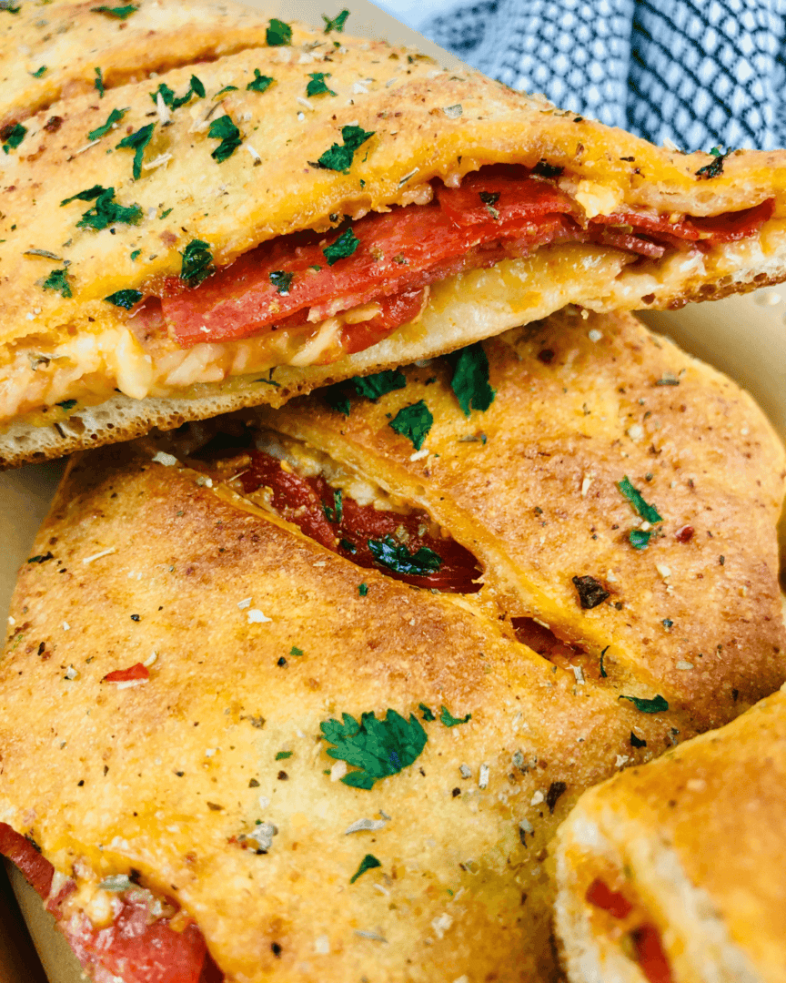 Close-up of a sliced Italian Stromboli filled with melted cheese and tomato, garnished with herbs, on a paper container.