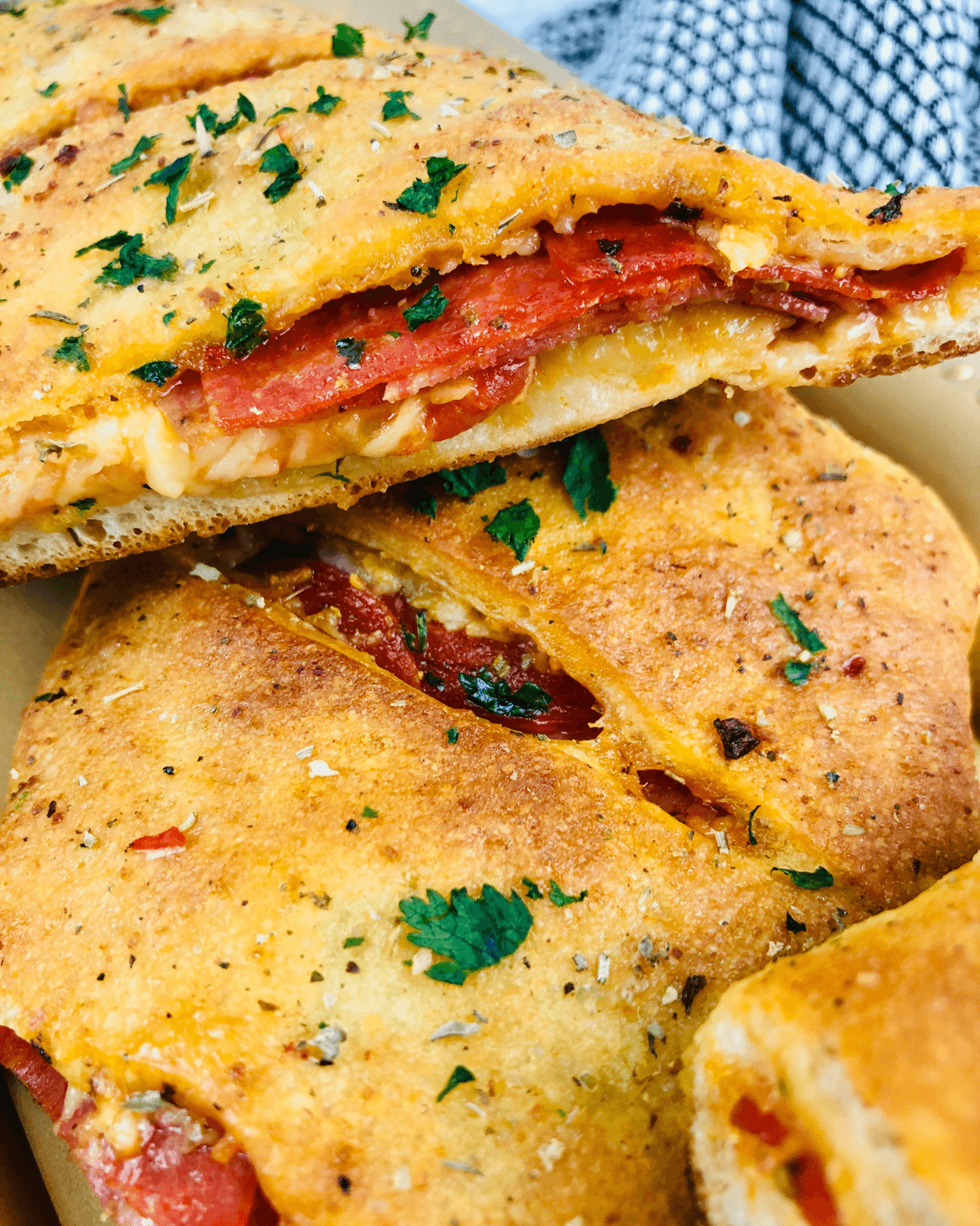 Close-up of a sliced Italian Stromboli filled with melted cheese and tomato, garnished with herbs, on a paper container.