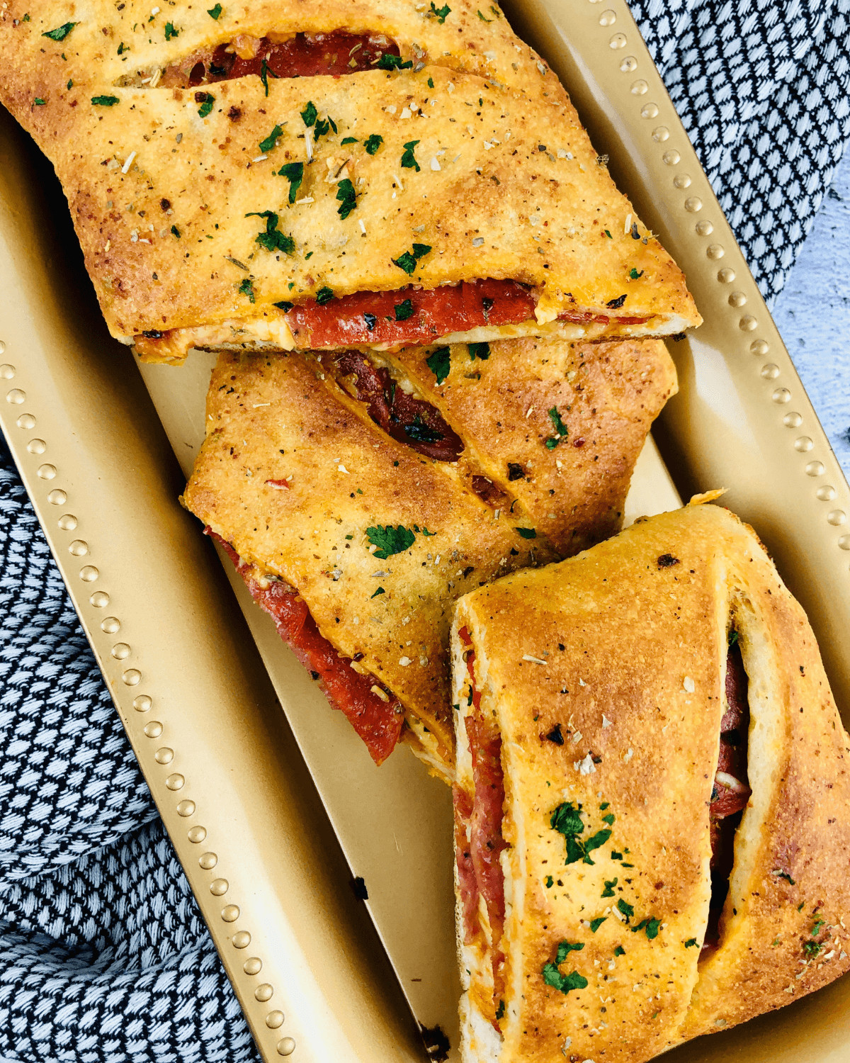 An Italian stromboli filled with pepperoni and cheese, garnished with herbs, served on a beige tray with a checkered napkin.