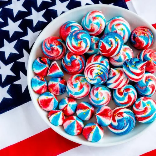 Bowl filled with red, white and blue meringue cookies with an American flag as the backdrop