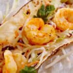 A soft tortilla taco filled with grilled shrimp, shredded cabbage slaw, fresh cilantro, and a tangy mango salsa. Enjoy these Shrimp Tacos with Mango Salsa served with a lime wedge on the side.