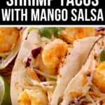Three Shrimp Tacos with Mango Salsa and slaw are arranged on a wooden surface, served with a lime wedge on the side.