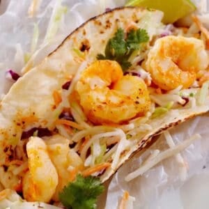 A shrimp taco with grilled shrimp, shredded cabbage slaw, cilantro, and a lime wedge on a toasted tortilla—perfect for pairing with Shrimp Tacos with Mango Salsa.