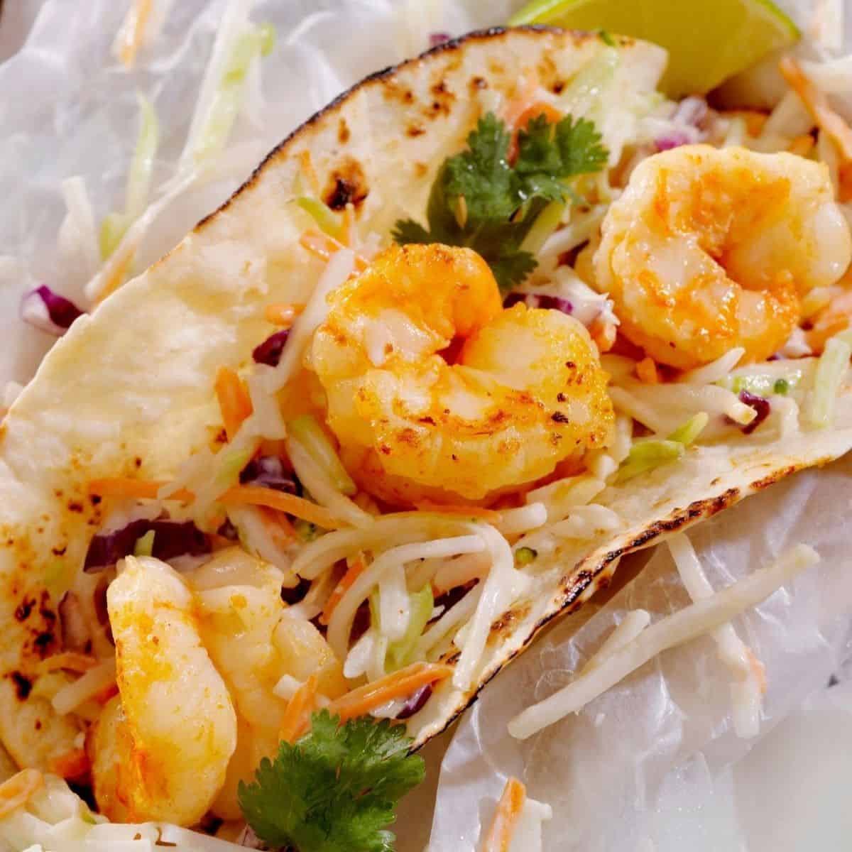 A shrimp taco with grilled shrimp, shredded cabbage slaw, cilantro, and a lime wedge on a toasted tortilla—perfect for pairing with Shrimp Tacos with Mango Salsa.