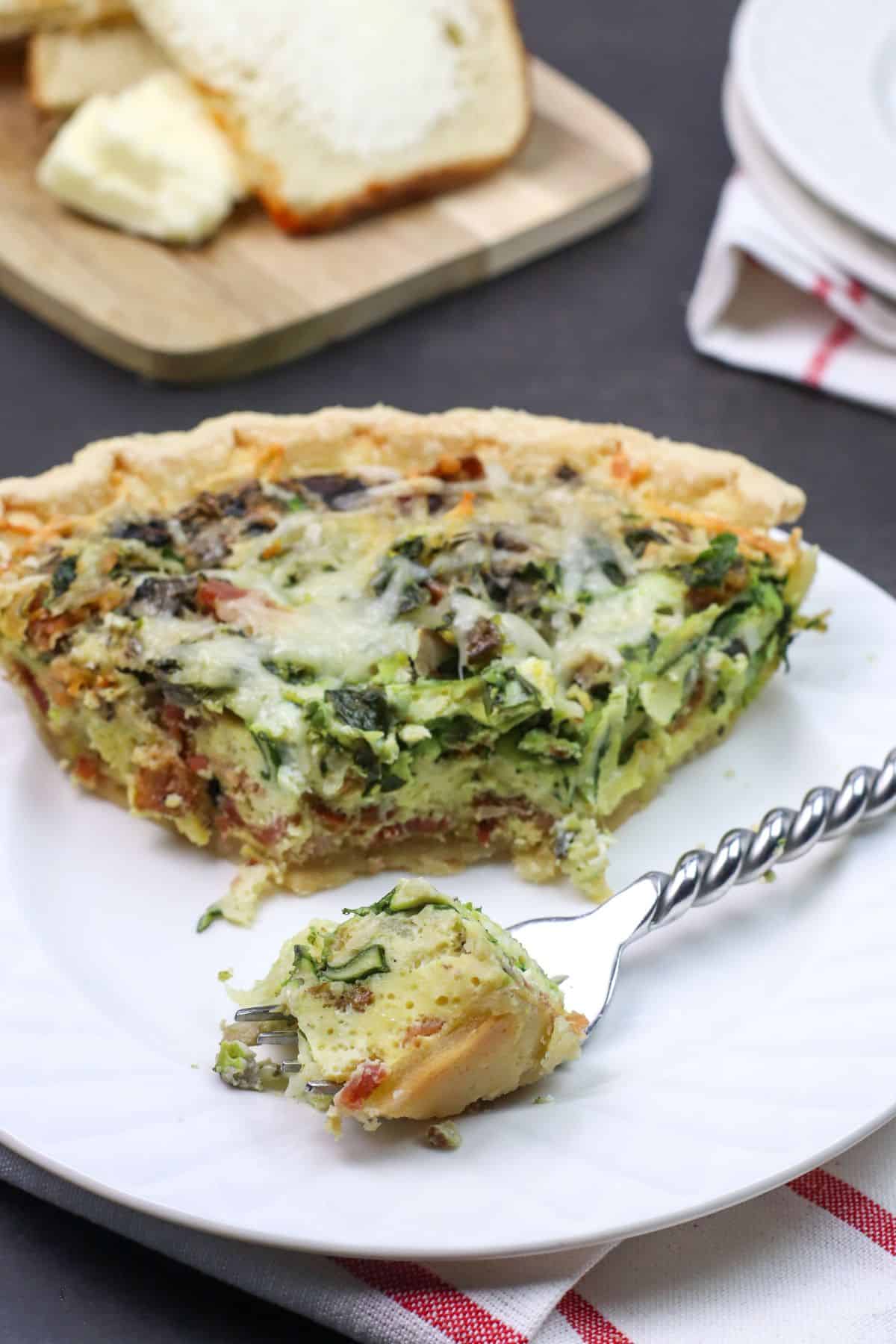 A slice with a bite on a fork, served on a white plate. Sliced bread and butter are visible in the background.