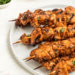 Three skewers rest on a white plate, garnished with chopped herbs.