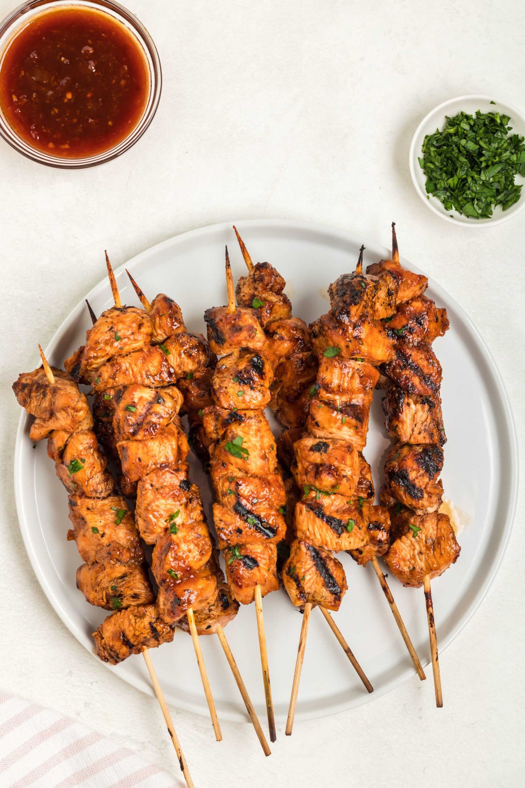 Grilled chicken on a stick on a plate with extra sauce on the side. 