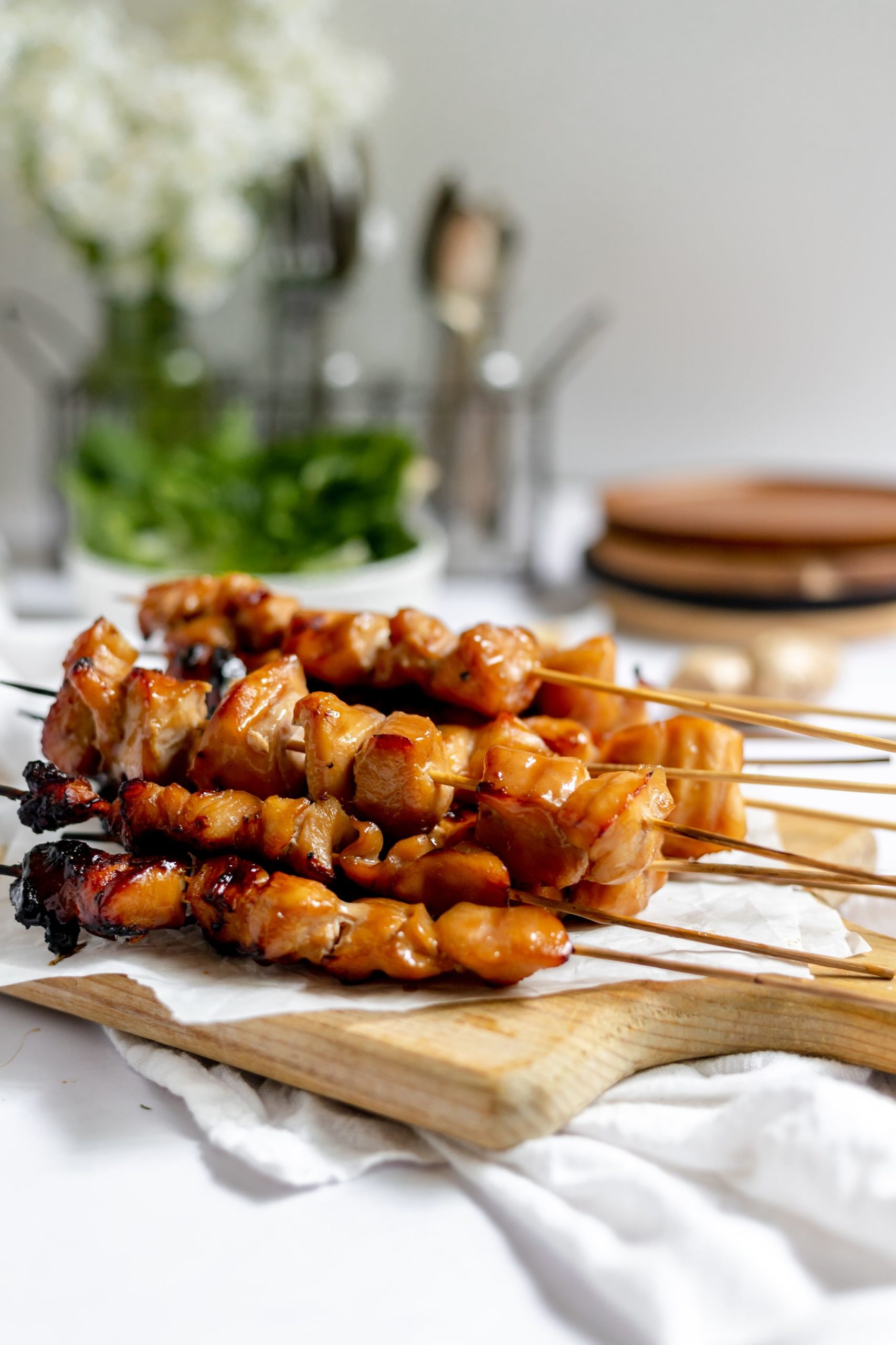 On a wooden cutting boards there are a stack of Teriyaki Chicken on a Stick. 