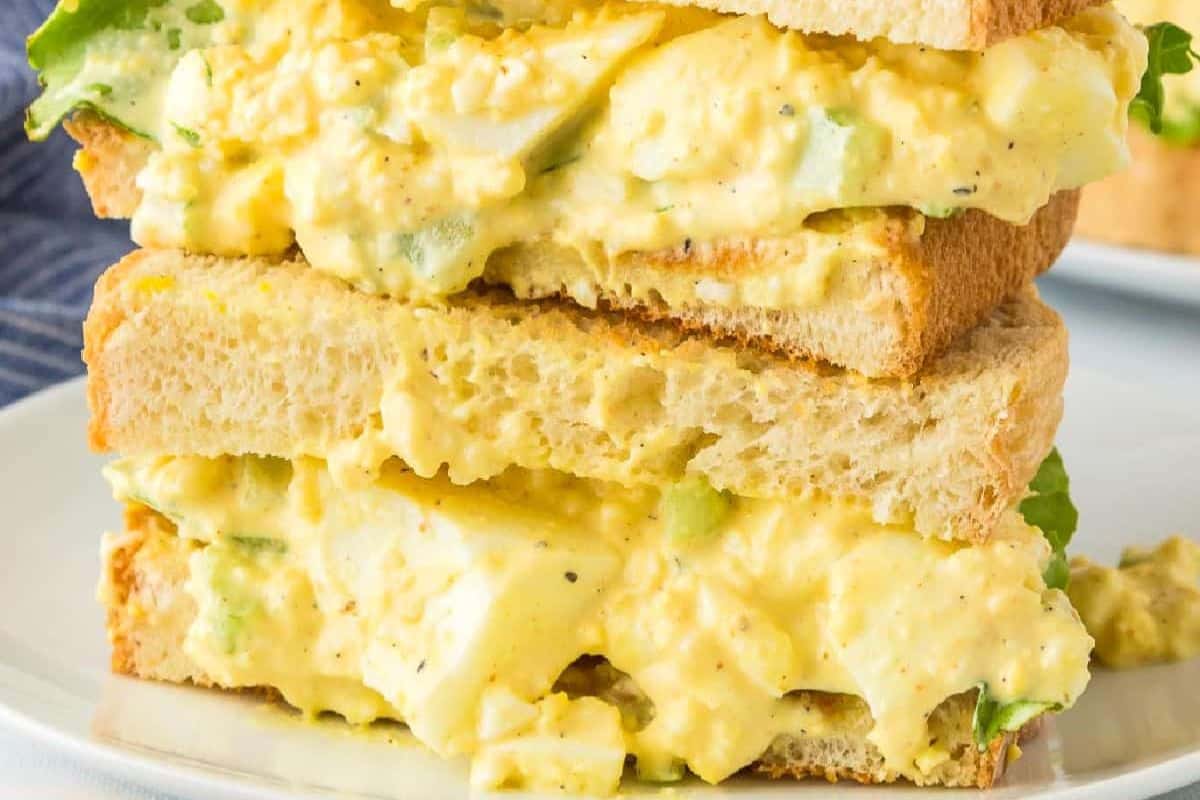 Close-up of an easy egg salad sandwich with lettuce on toasted bread, cut in half and stacked on a white plate.