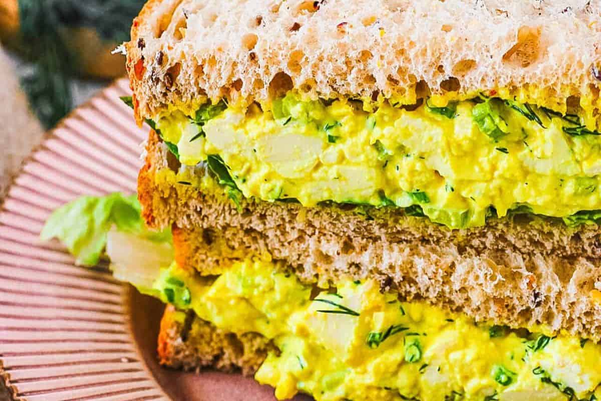 Close-up of a vegan egg salad sandwich with diced vegetables on whole-grain bread, displayed on a brown plate—a delicious example of easy egg salad recipes.