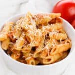 A bowl of pasta topped with cheese and rich tomato, tossed in a creamy vodka cream sauce.
