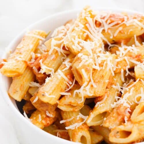 A white bowl filled with rigatoni pasta covered in rich vodka cream sauce and topped with grated cheese.