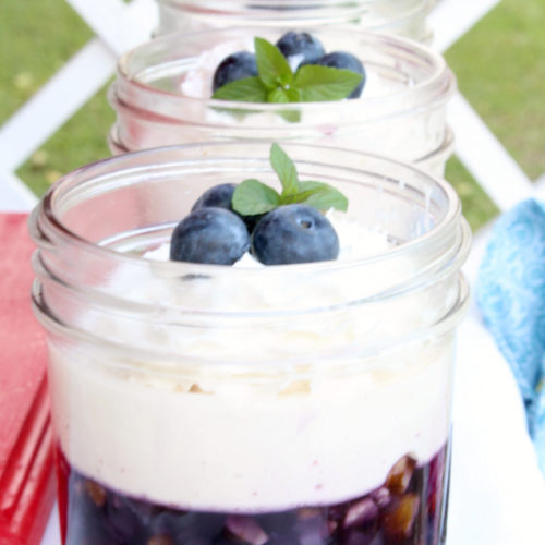 small mason jars filled with blueberry jello topped with whipped cream and blueberries