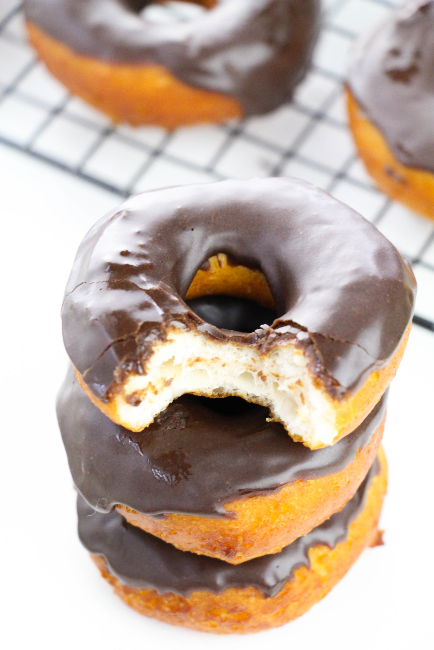 A stack of Chocolate Glazed Biscuit Donuts with a bite taken out.