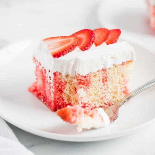 Strawberry jello cake with white frosting and topped with fresh strawberries