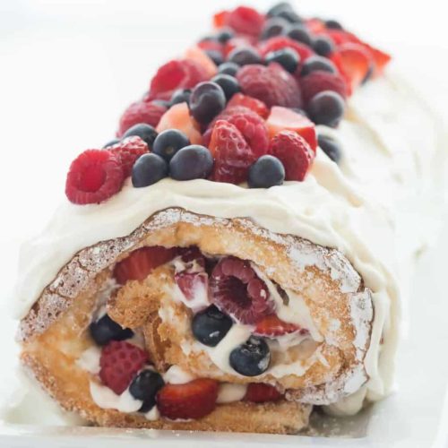 a rolled angel food cake with fresh raspberries and blueberries