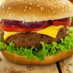 A close-up view of an air fryer hamburger patty with lettuce, tomato, red onion, and a beef patty, topped with a sesame seed bun.