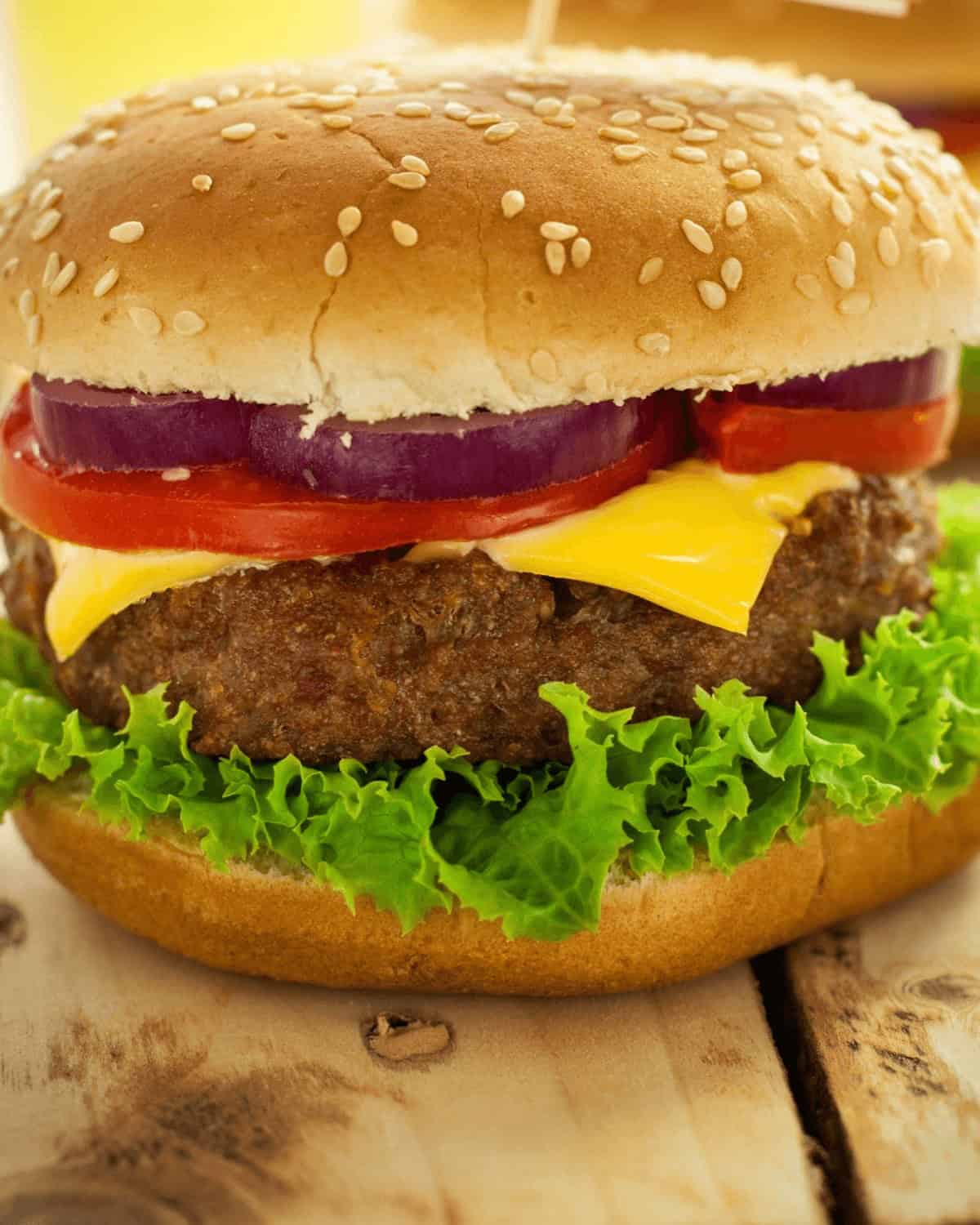 A close-up view of an air fryer hamburger patty with lettuce, tomato, red onion, and a beef patty, topped with a sesame seed bun.