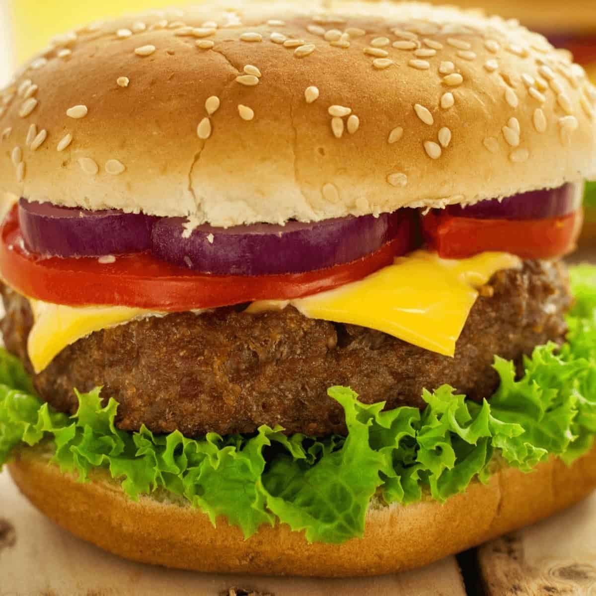 A close-up of a cheeseburger with lettuce, tomato, red onion, melted cheese, and a sesame seed bun. The succulent air fryer hamburger patties add an extra layer of crispiness to this mouthwatering delight.