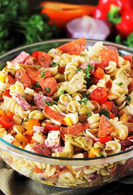 Glass bowl filled with antipasto pasta salad with fresh tomatos and onions