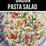 A bowl of Bacon Pasta Salad with Ranch Dressing, featuring rotini pasta, cherry tomatoes, peas, and parsley. A wooden spoon is partially visible in the background.