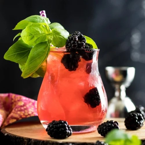 A glass of Blackberry Basil Julep garnished with mint leaves and blackberries