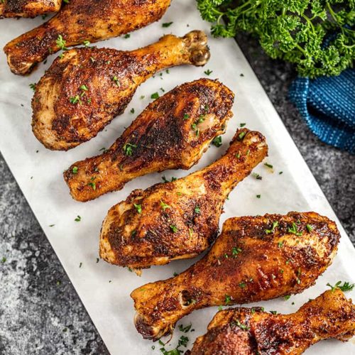 A plate of perfectly cooked grilled chicken drumsticks garnished with parsley