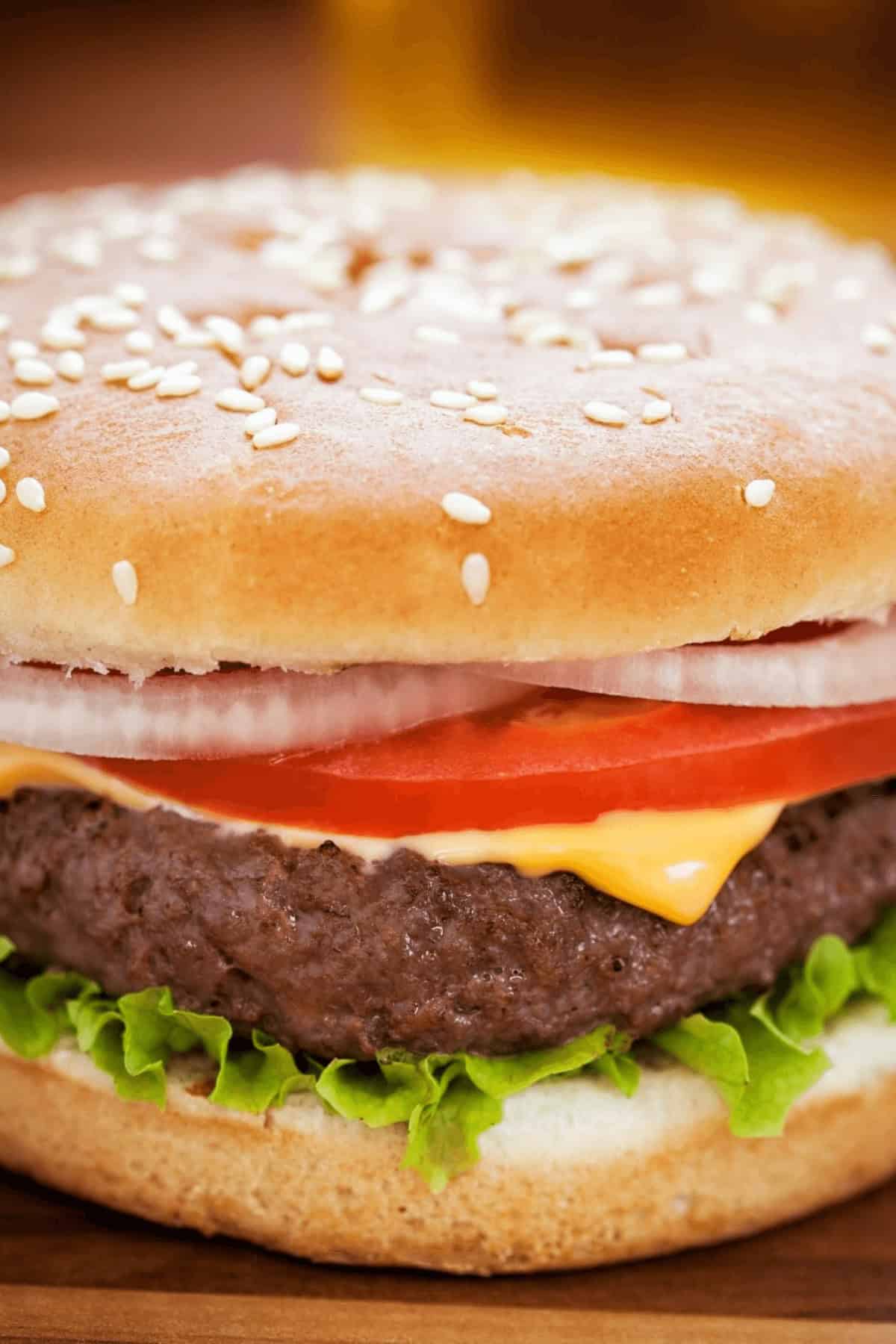 A close-up of a Cast Iron Burger featuring a sesame seed bun, lettuce, a beef patty, melted cheese, tomato slices, and onion rings.