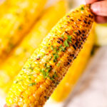 Holding an ear of cooked corn.