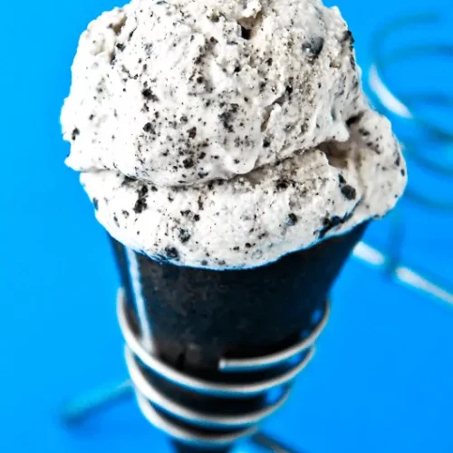 One scoop of cookies and cream ice cream sits on top of a cone made of crushed oreos