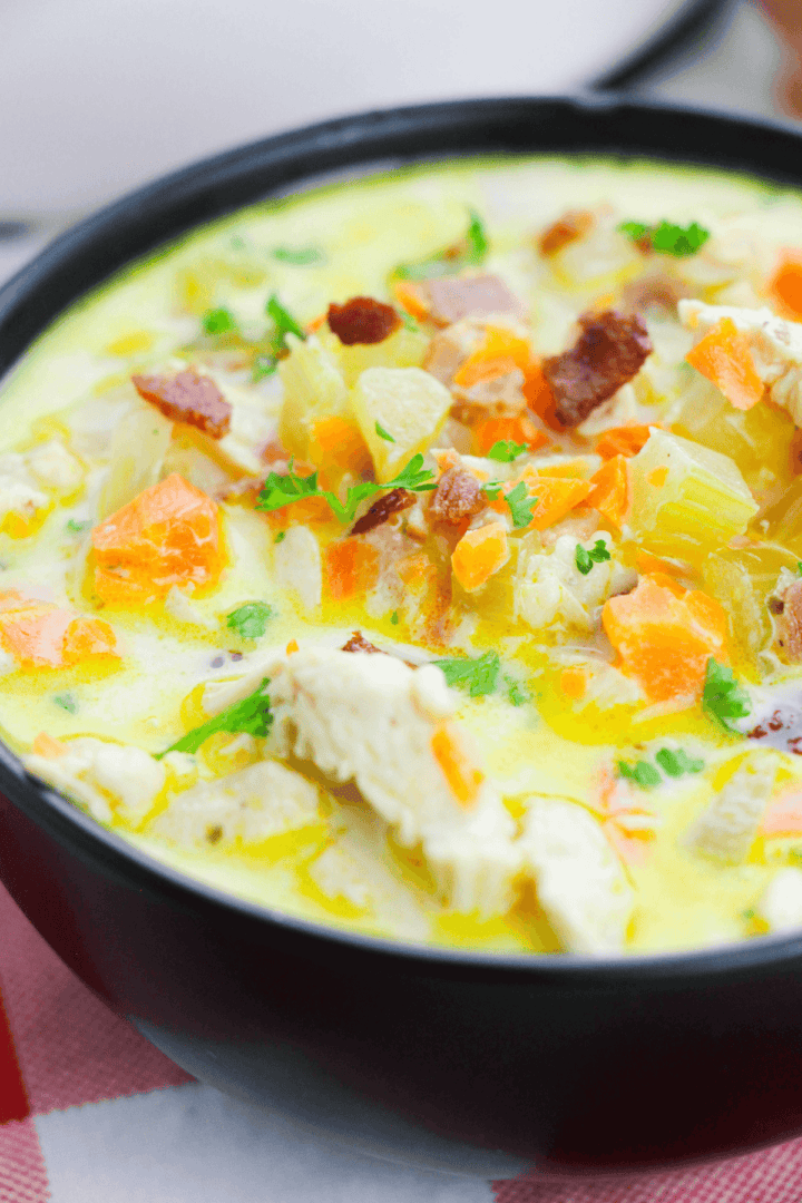 Close-up of a bowl of creamy cracked chicken soup with chunks of chicken, carrots, and garnished with parsley.