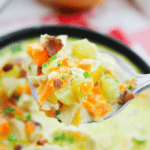 A spoonful of Cracked Chicken Soup, rich and creamy with vegetables like carrots, potatoes, and herbs, is held above a bowl of the same comforting soup.