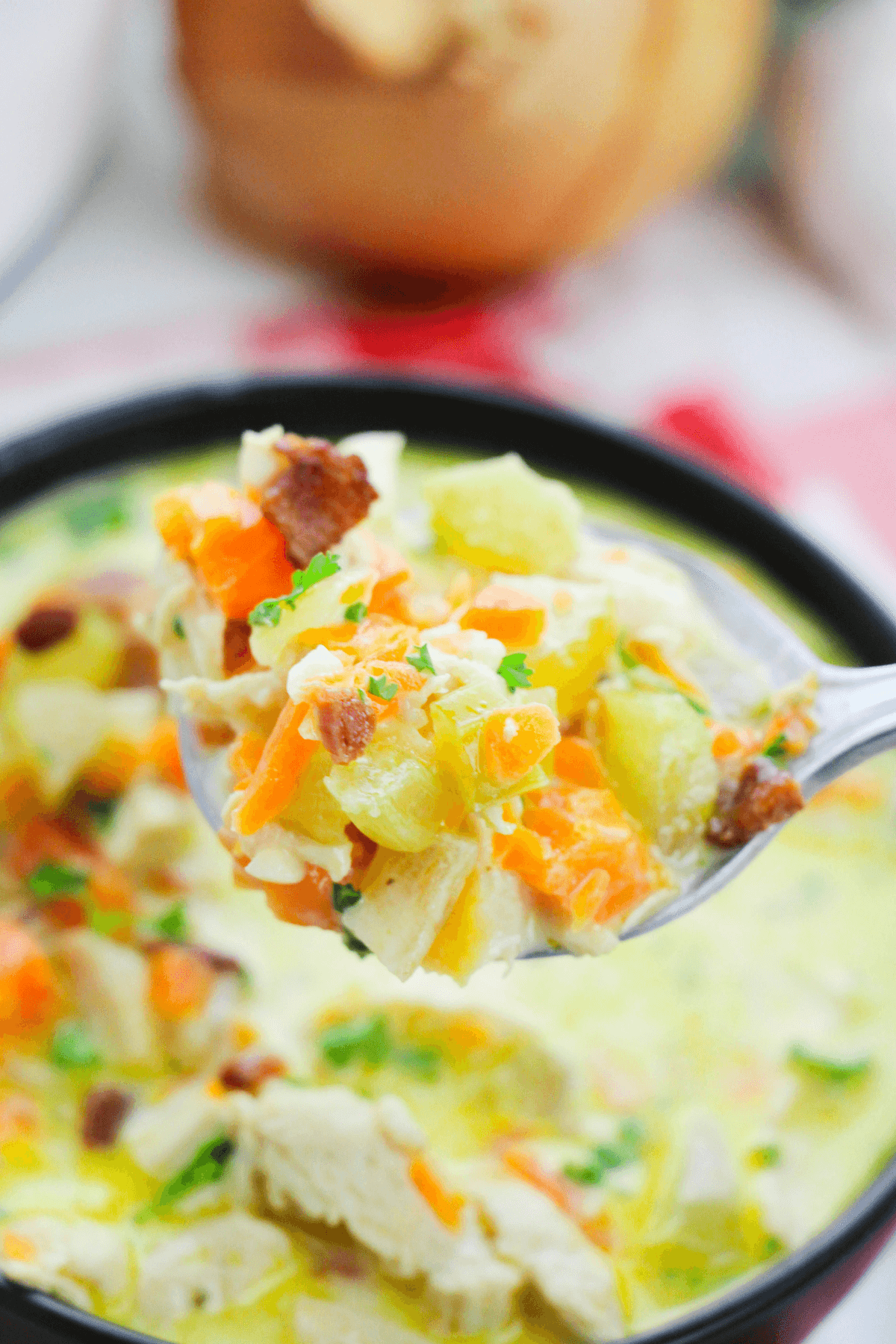 A spoonful of Cracked Chicken Soup, rich and creamy with vegetables like carrots, potatoes, and herbs, is held above a bowl of the same comforting soup.