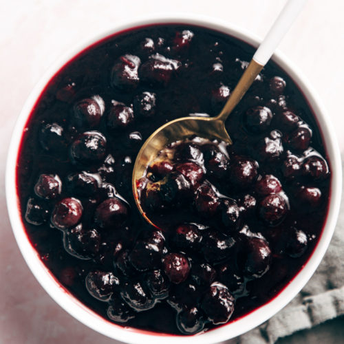 Homeade blueberry sauce in a white bowl with a spoon sticking in it