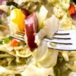 A close-up of a fork holding a bite of Fried Cabbage and Sausage with bell pepper, with more of the tasty dish visible in the background.