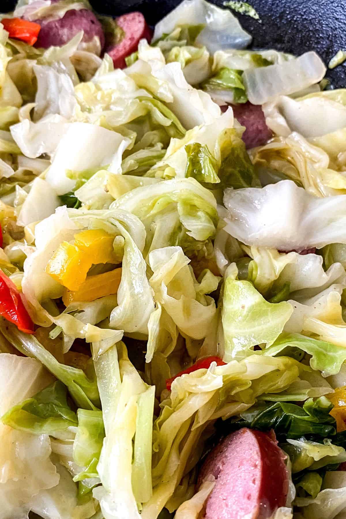 Close-up of Fried Cabbage and Sausage mixed with sliced sausage and pieces of red and yellow bell peppers.