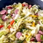 A skillet filled with hearty Fried Cabbage and Sausage, mixed with tender cabbage, sliced sausage, and colorful pieces of red and yellow bell pepper.