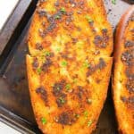 A piece of homemade toast on a baking tray, topped with herbs and browned bits of garlic.