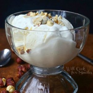 A glass bowl of white ice cream with hazelnuts on it