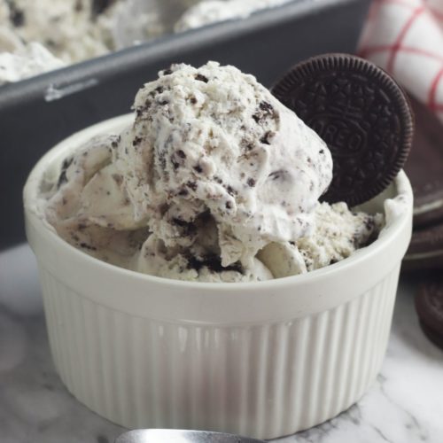 A white ramican holds several scoops of oreo ice cream, garnished with a whole oreo