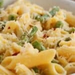 A bowl of Lemon Asparagus Pasta featuring penne mixed with asparagus pieces, topped with shredded cheese and a sprinkle of red pepper flakes.