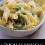 A white bowl filled with Lemon Asparagus Pasta, featuring penne, asparagus, green peas, and grated cheese. Lemon slices and asparagus are in the background. Text reads: "Lemon Asparagus Pasta.