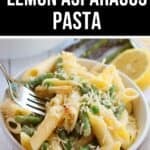 Bowl of creamy Lemon Asparagus Pasta topped with grated cheese, with a fork, fresh asparagus, and a lemon half in the background.