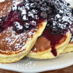 Lemon Pancakes with Blueberry Compote on a white dish with powdered sugar.